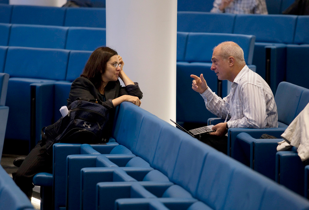 Two people sitting in different rows of an almost empty lecture hall, while talking