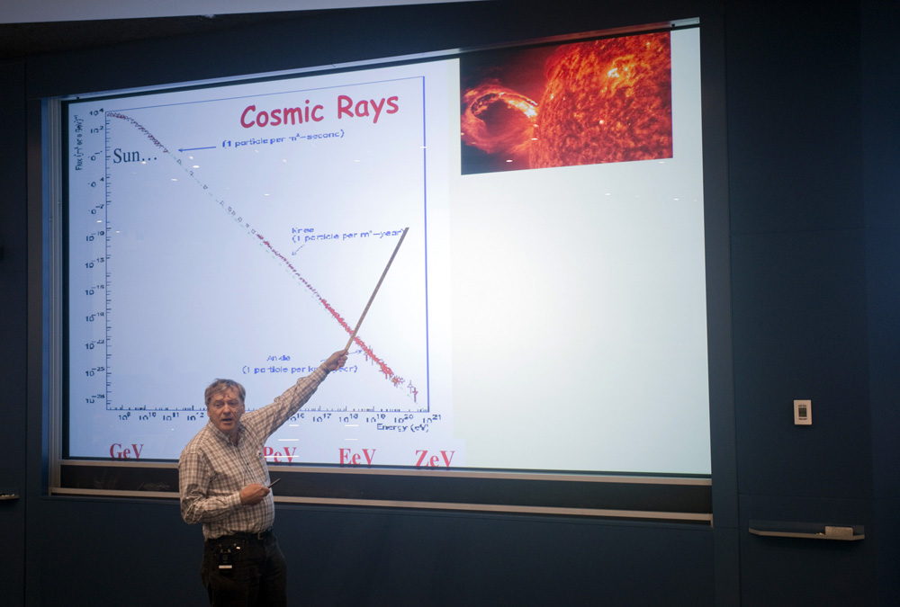 Man pointing to a projected slideshow titled Cosmic Rays