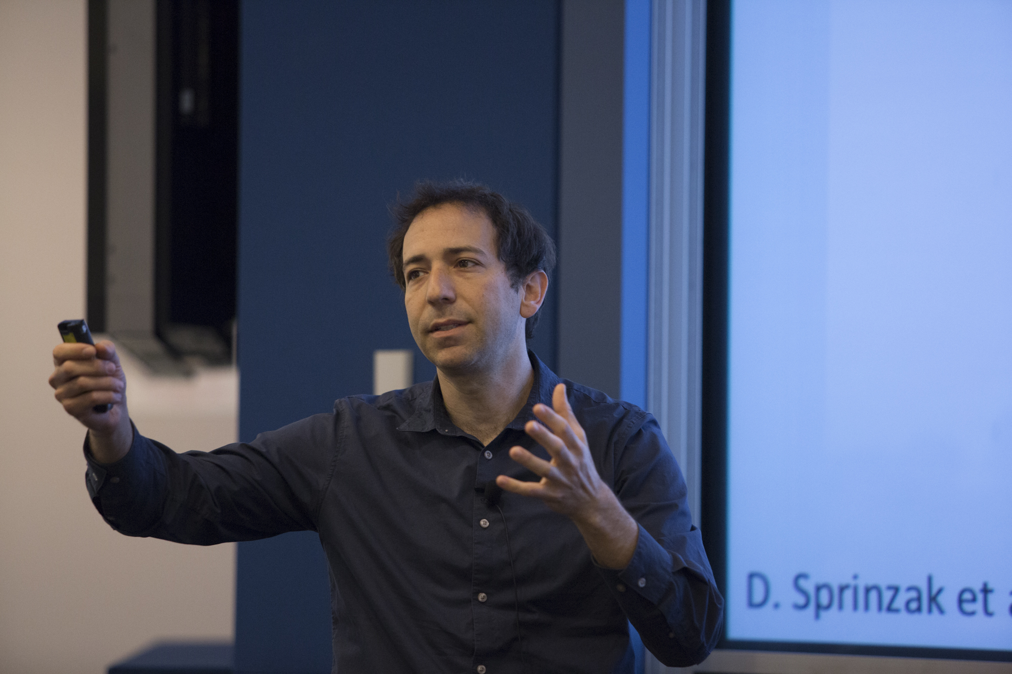 Man standing while talking, in front of a slideshow that says D. Sprinzak et al