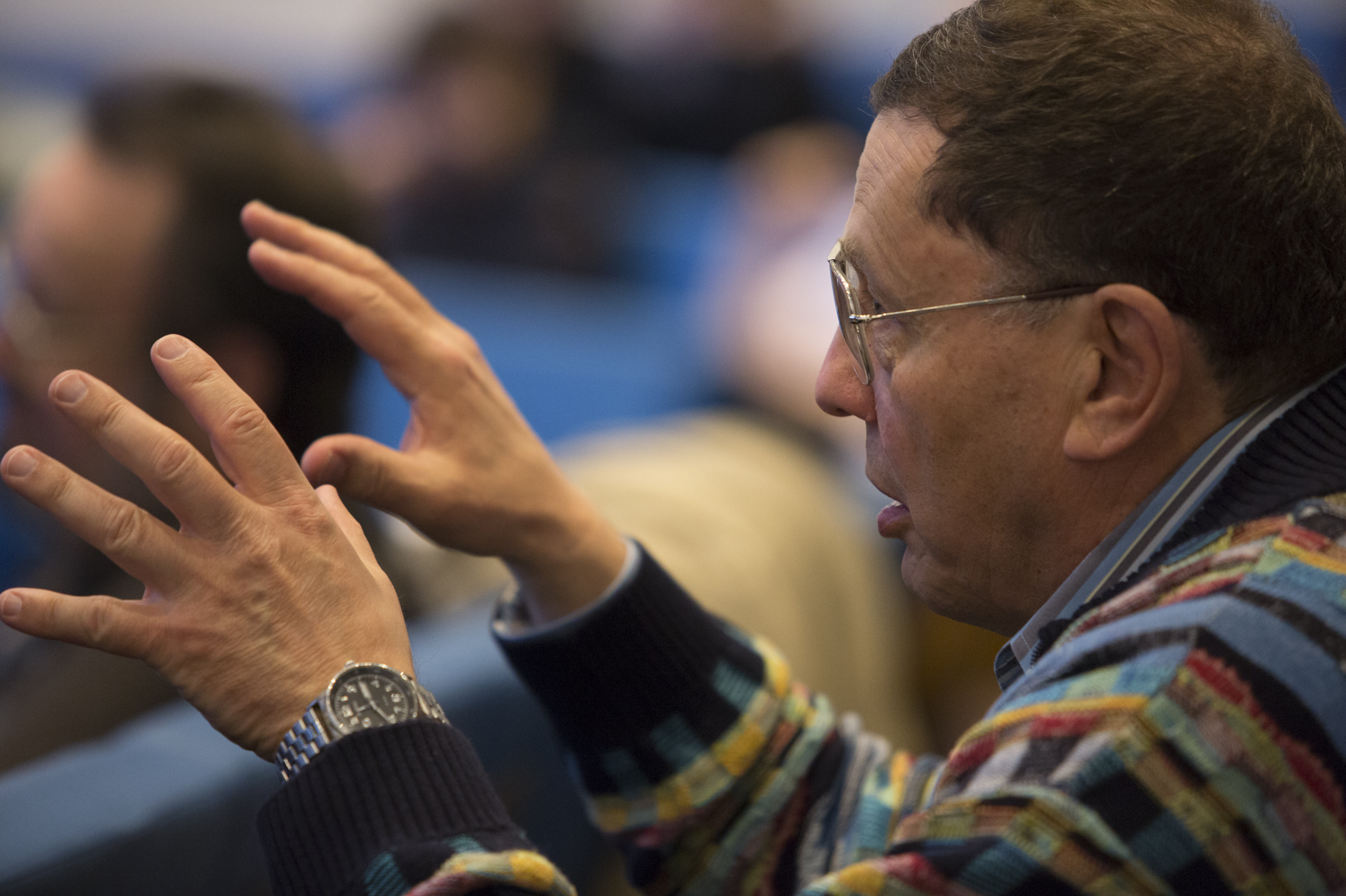 Man gesticulating with both hands as he sits in a lecture hall