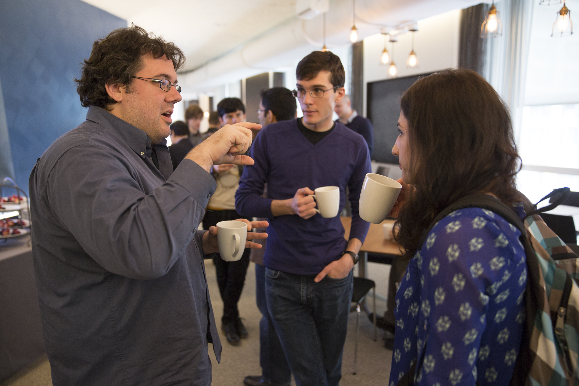 Three standing people holding mugs while talking