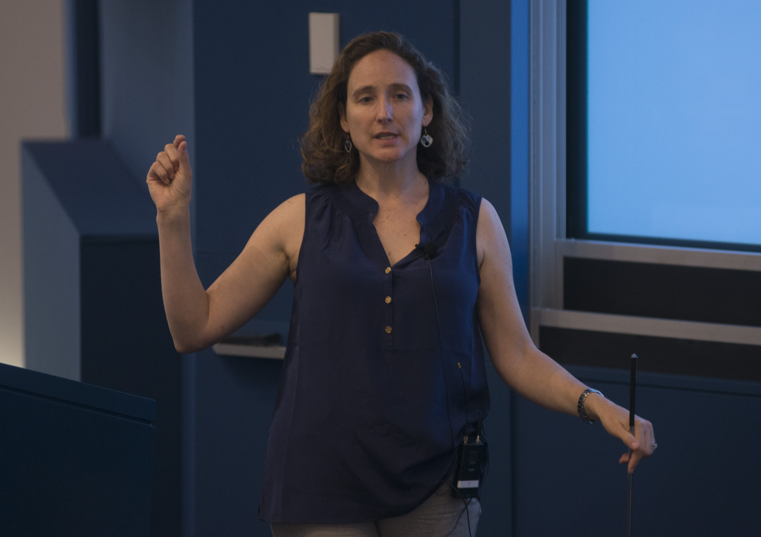 Woman standing by a lectern, as she gesticulates with her right hand