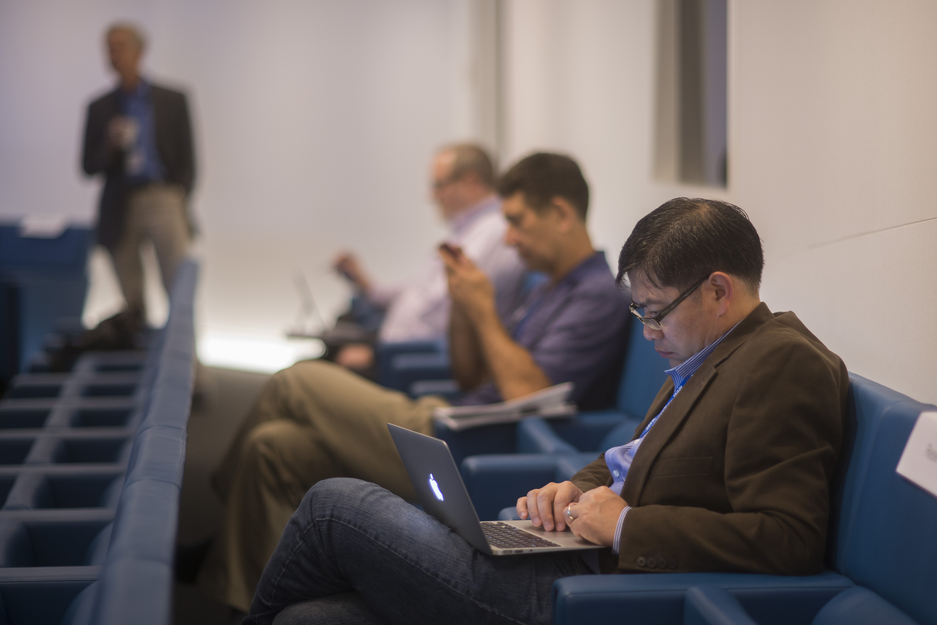 Three men in the back row of a lecture hall on their personal electronic devices