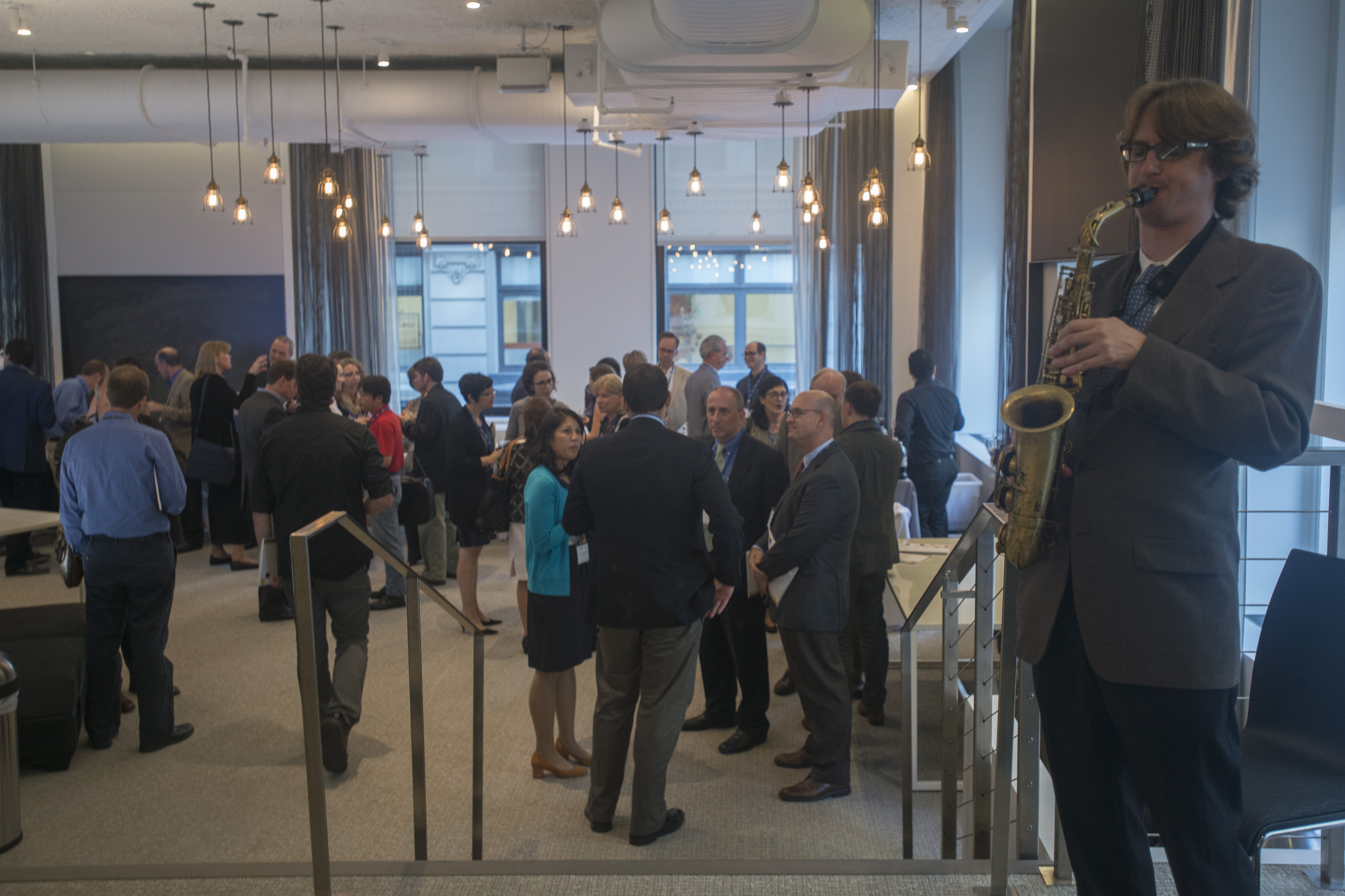 Man playing a saxophone at the top of a few steps as people down the steps stand and mingle