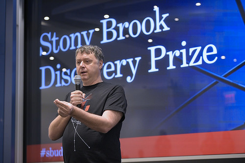 Man standing on a stage with the words Stony Brook Discovery Prize behind him