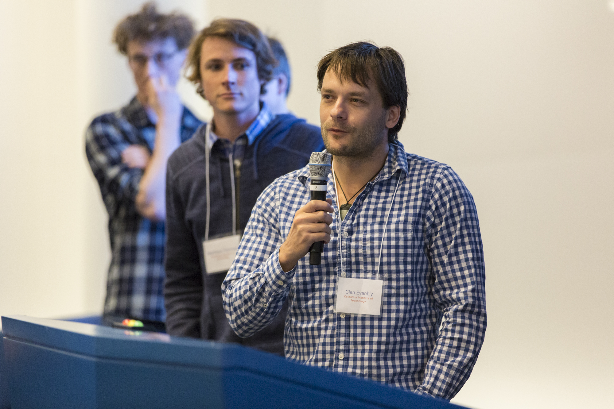 Man speaking into a microphone as he stands behind a lectern and people line up behind him