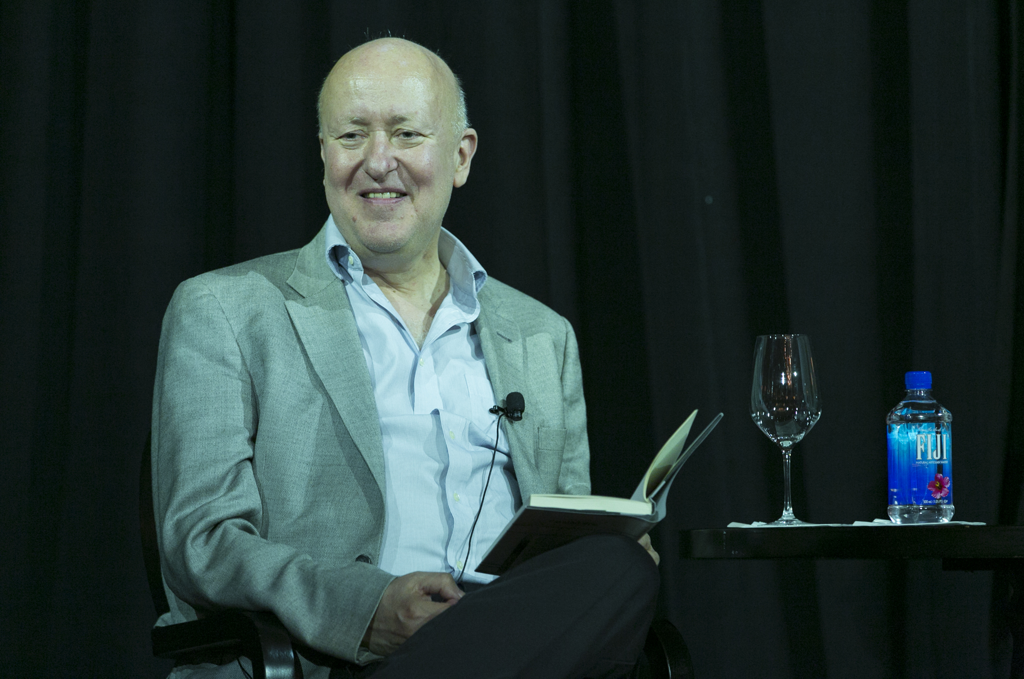 Man sitting on a stage as he holds a book on his leg