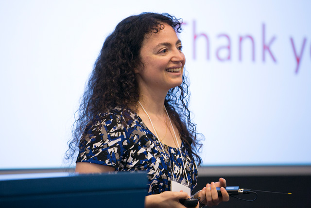Woman standing next to a lectern as she's smiling and presenting a slideshow