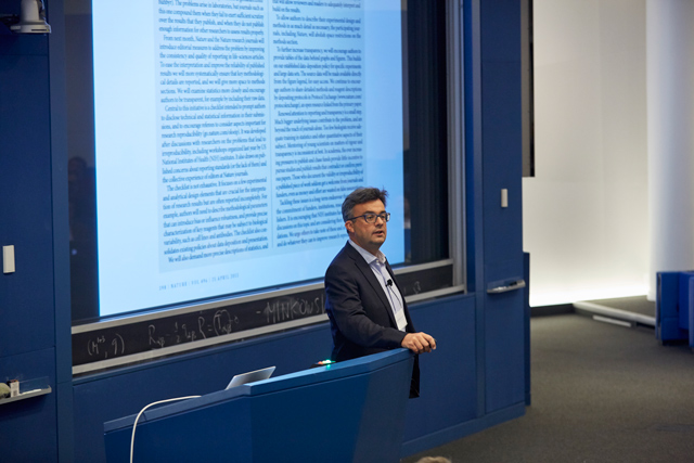 Man standing in front of a presentation as he places his hand on a lectern