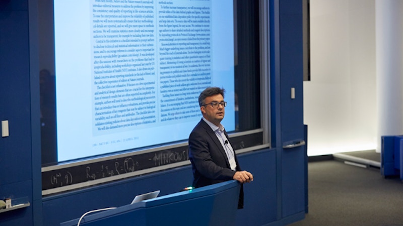 Man standing in front of a presentation as he places his hand on a lectern