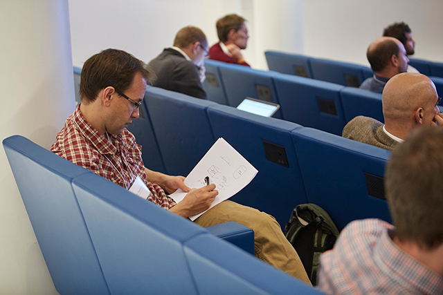 Man sitting in a corner of a lecture hall while writing on a piece of paper