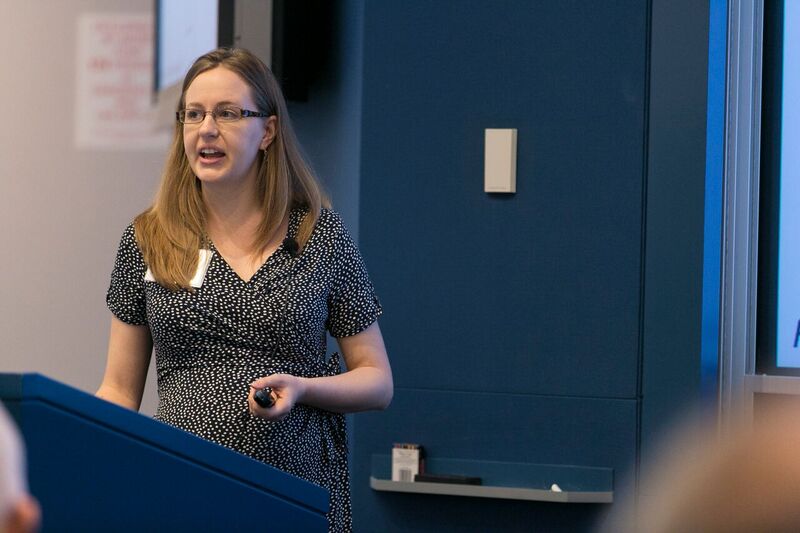 Lisa Giacomo of Stanford University stands behind a blue lectern as he presents a slideshow