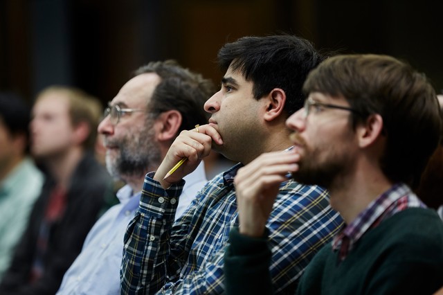 Three men sitting next to each other as two of them touch their chins