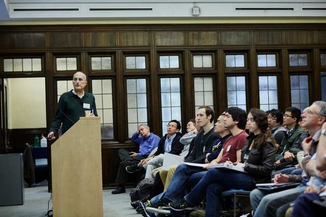 Man standing to the side of a lectern as a classroom of people watch