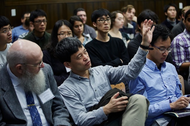 Lecture hall full of people sitting and looking forward as one man talks and gesticulates with his left hand
