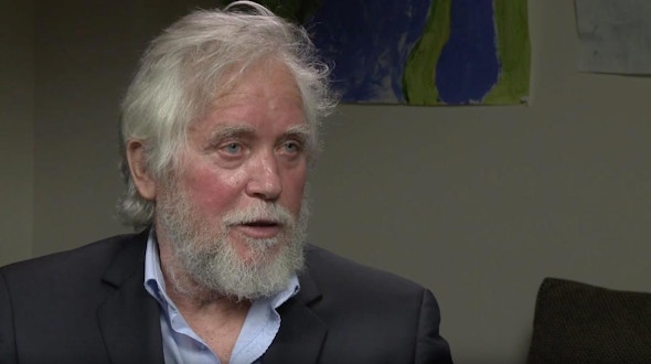 Endre Szemerédi sits in front of a white wall