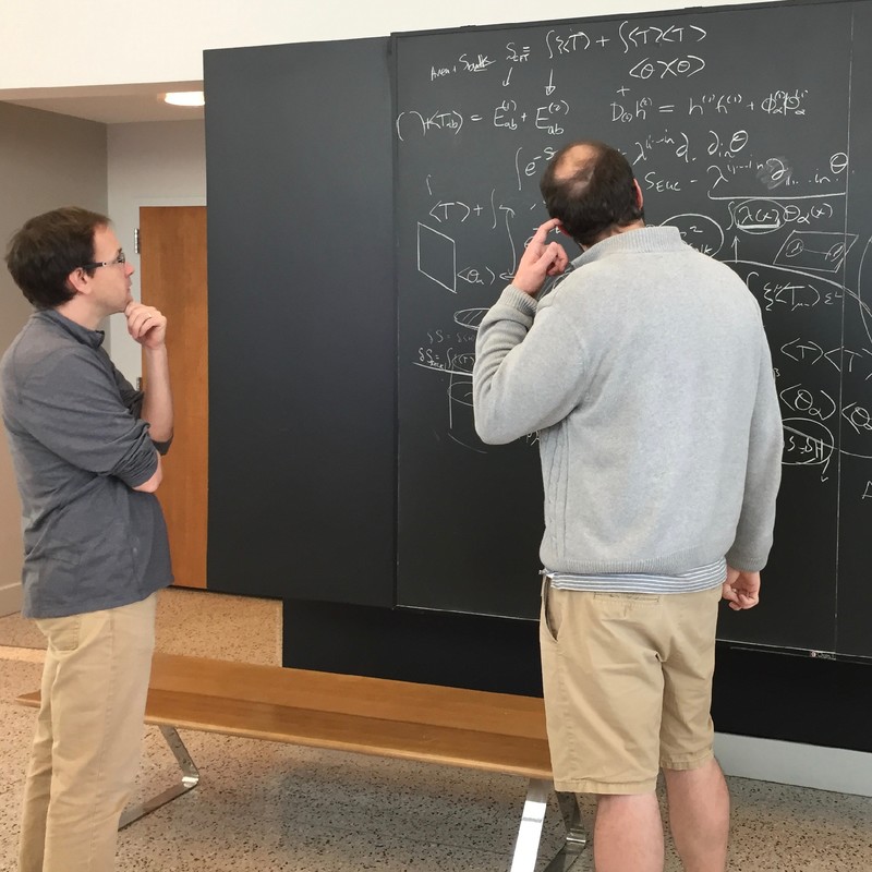 Two people standing and looking at math on a chalkboard wall