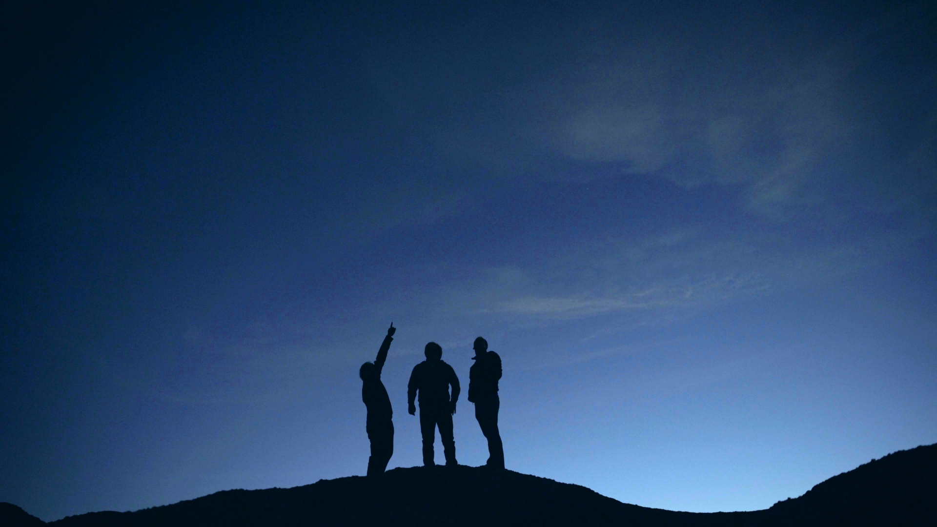 Silhouette of three men on top of rock against background of starry sky