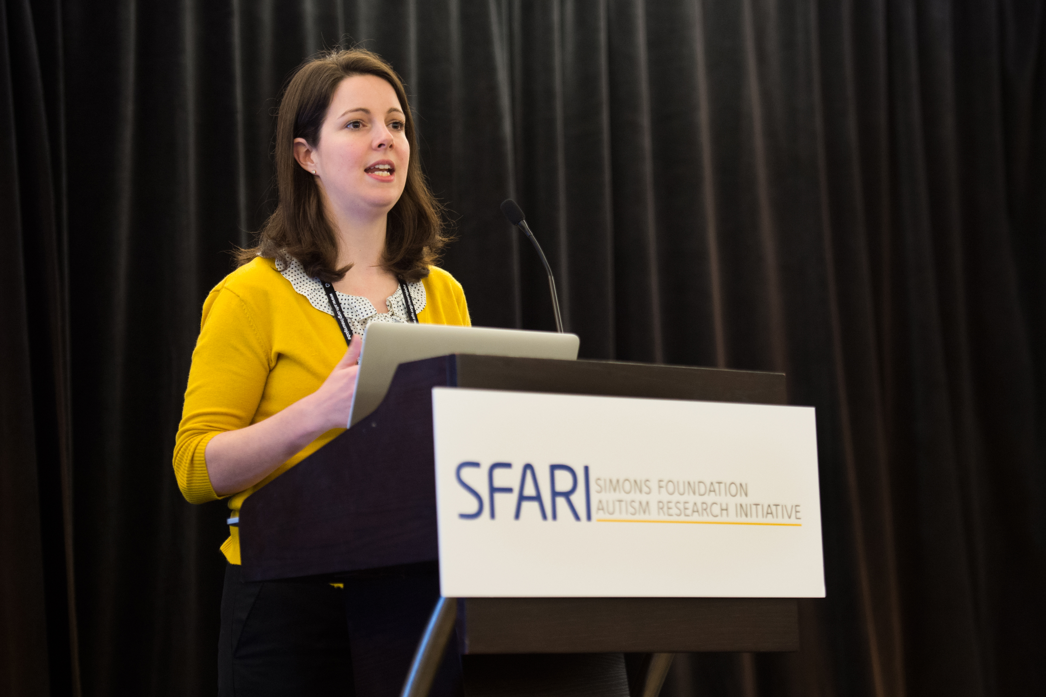 Woman talking behind a podium labeled SFARI Simons Foundation Autism Research Initiative