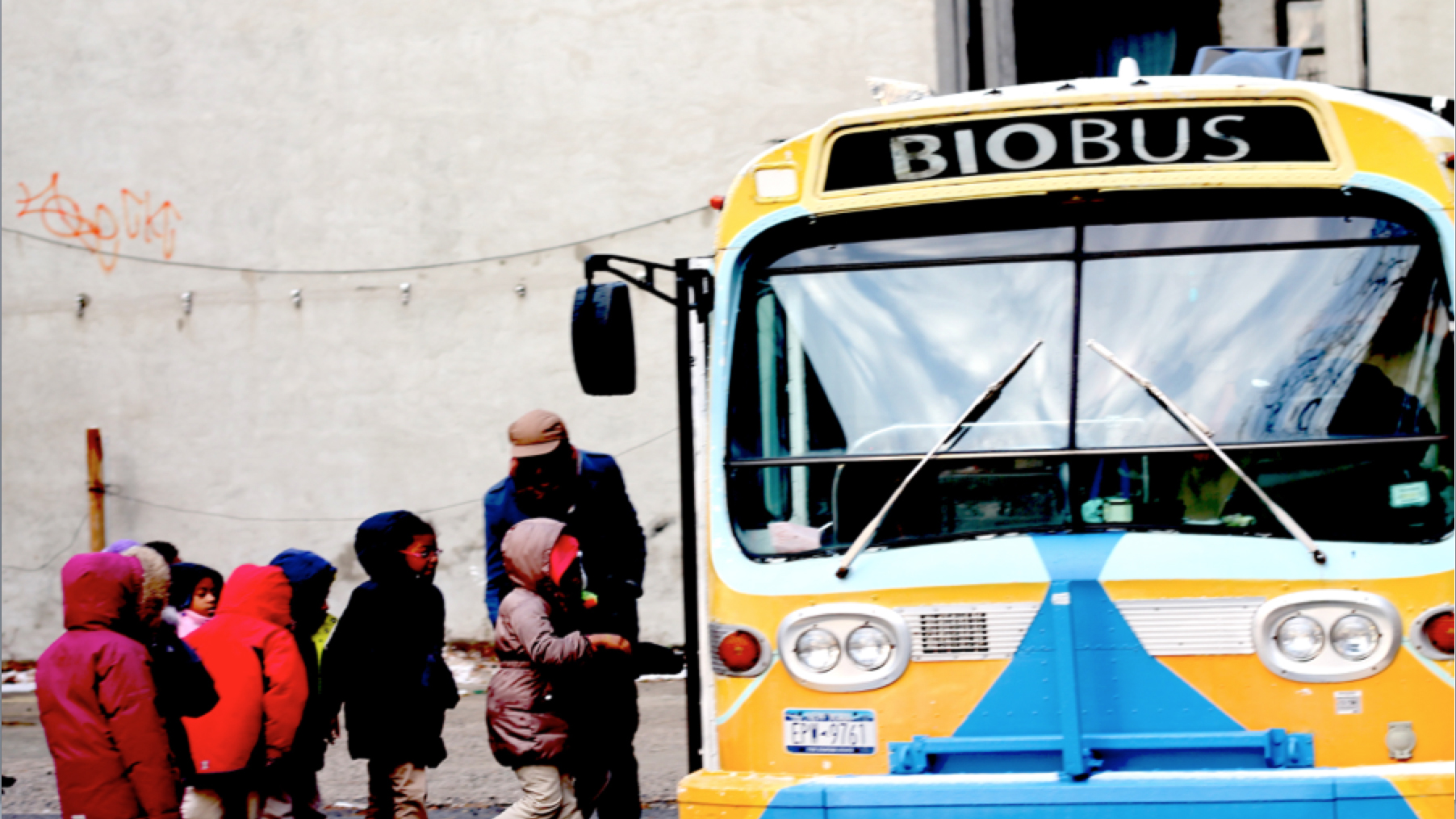Adult helps group of 8 young kids board a school bus labelled biobus