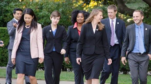 Seven people in business attire walking and talking together