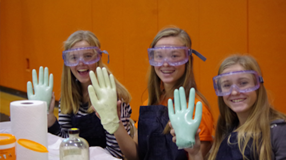 Three women in goggles holding up foam polymer hands