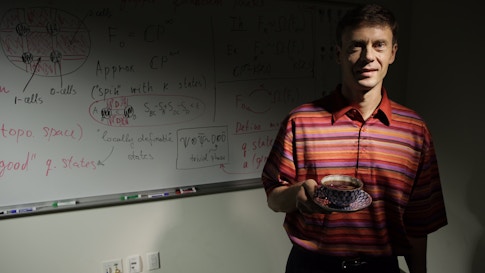 Alexei Kitaev holding a cup of tea while standing in front of a whiteboard