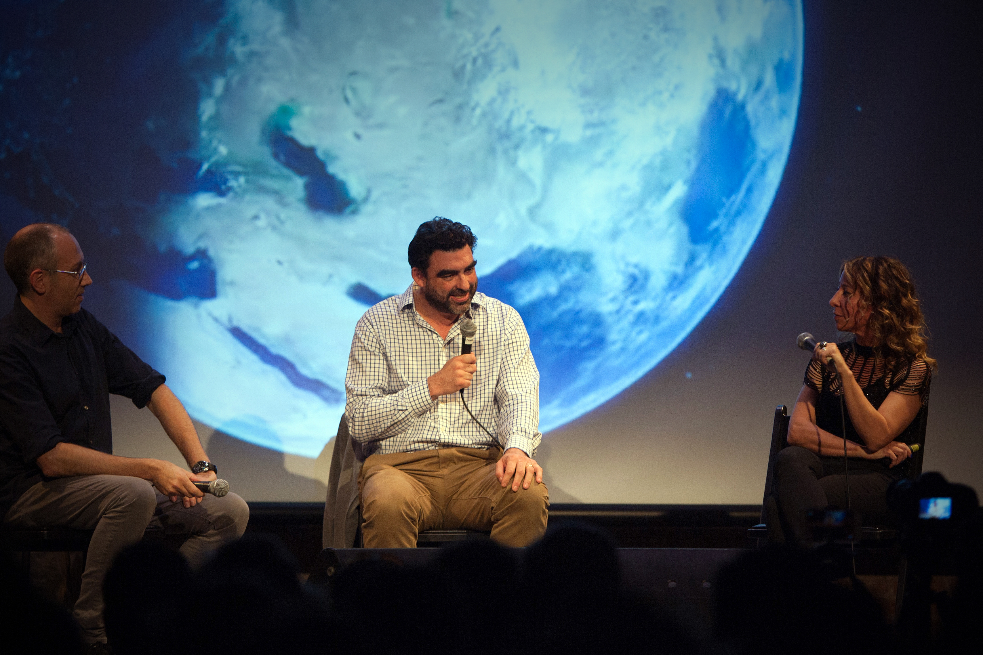 Three people sitting on a stage and talking into microphones