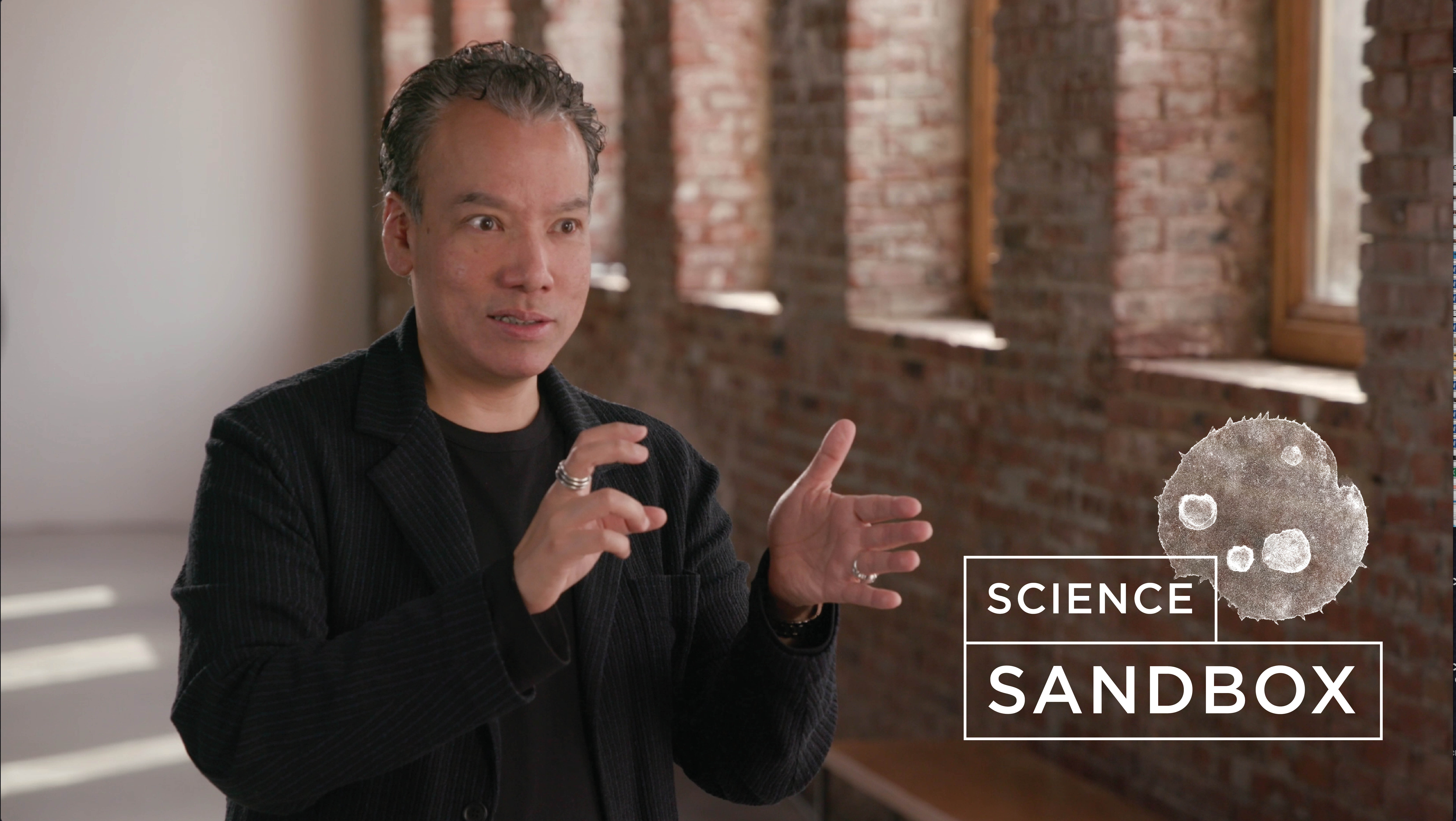 Robert Lue talking in an empty hallway with the Science Sandbox logo pasted next to her