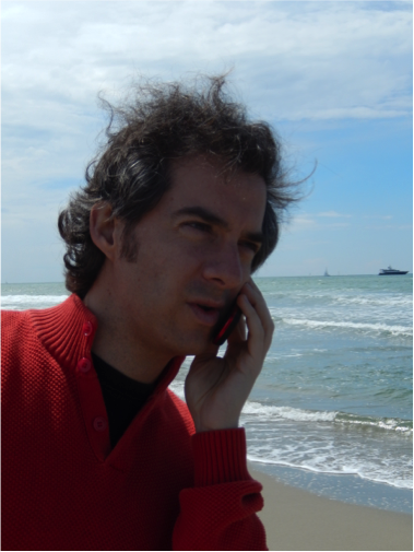 Giulio Biroli talking on a red flip phone by the beach