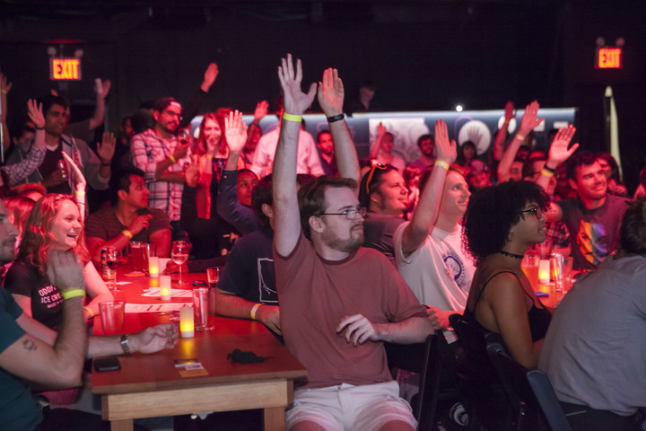 Audience in a candlelit room raise their hands