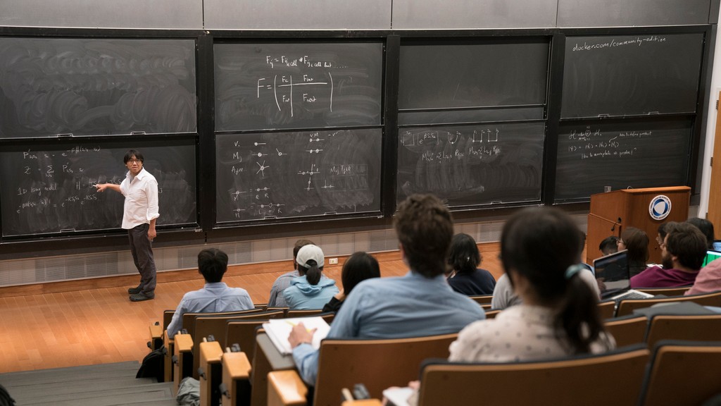 Man pointing to sliding chalkboard in front of a lecture hall
