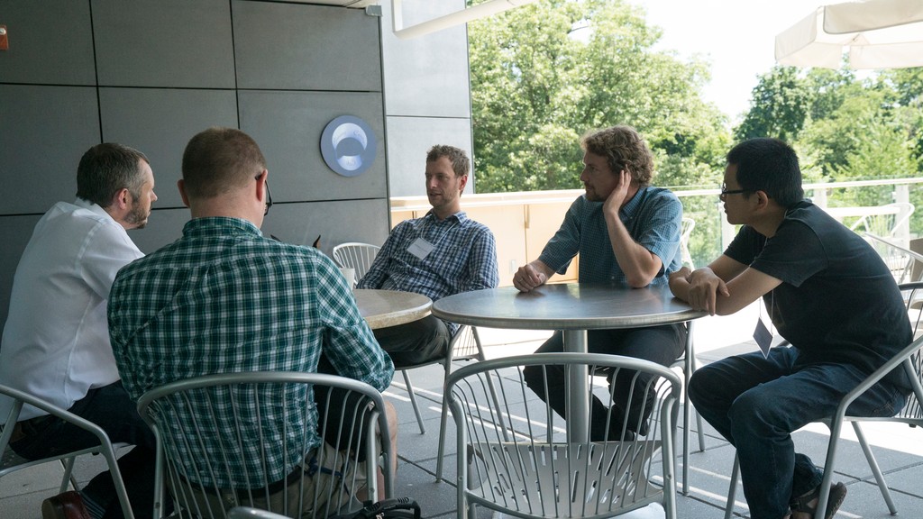 Five people sitting on two round tables outside
