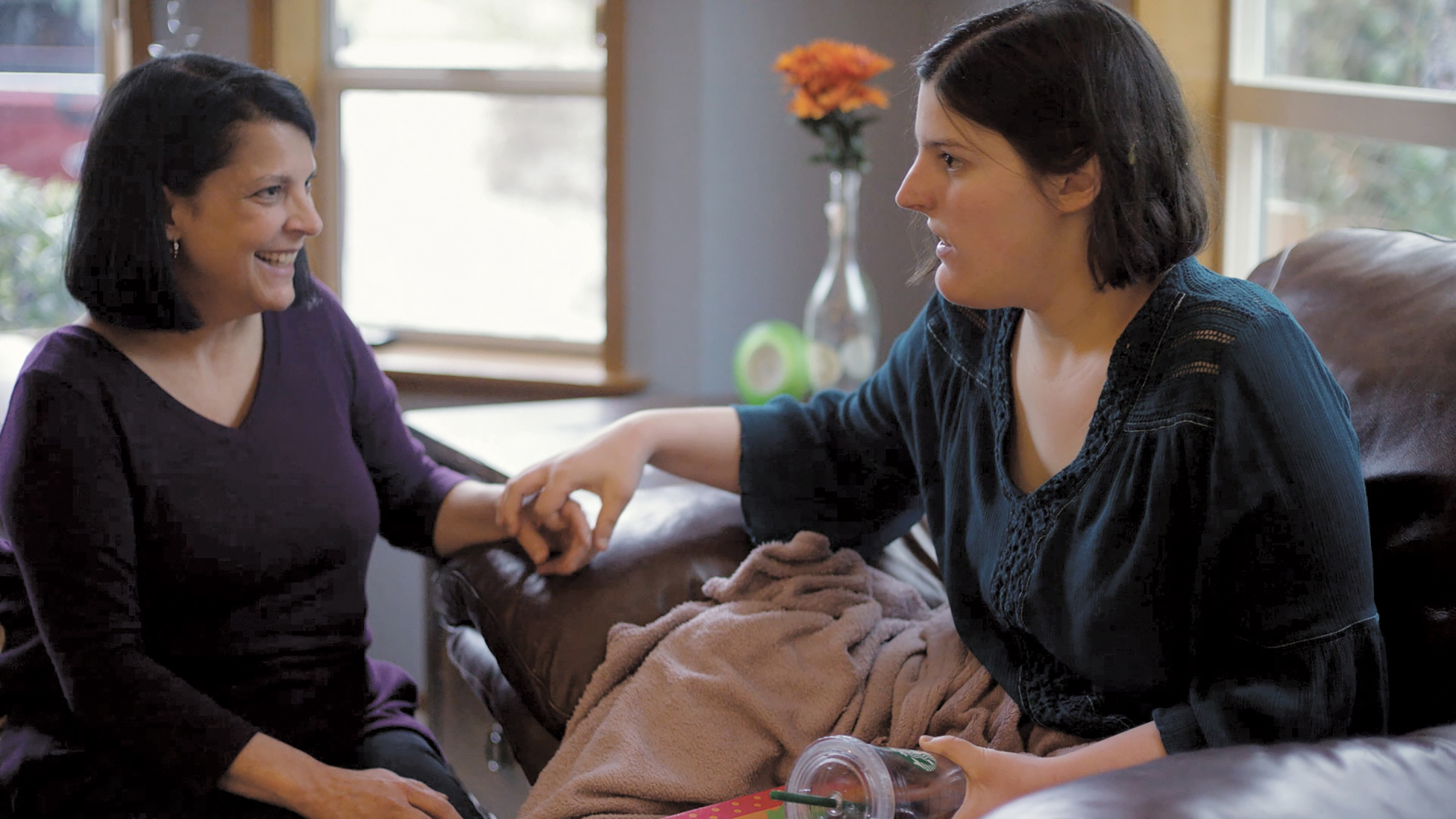 Woman sitting on a couch touching another sitting woman's hand