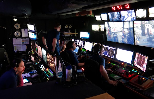 People sitting behind room full of monitors