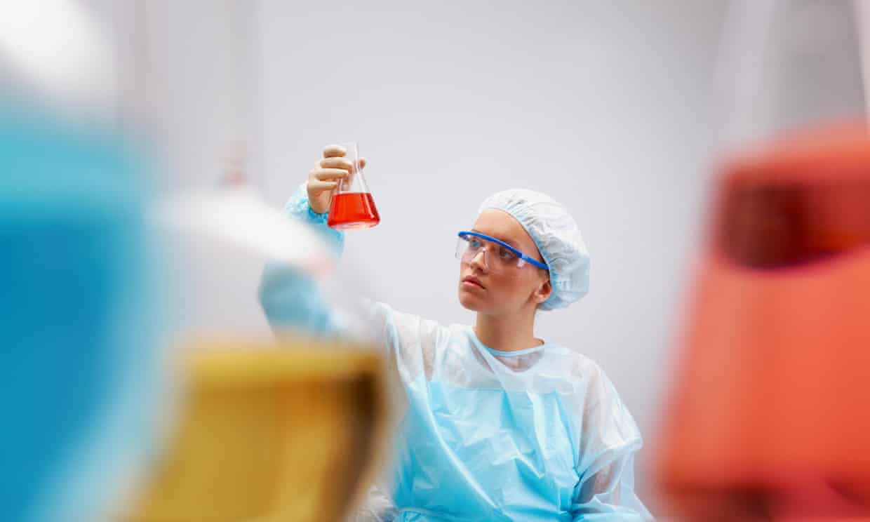 A woman lab worker looks at a flask with red liquid