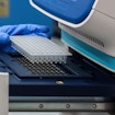 A photograph of DNA samples being placed in a PCR Machine by a gloved hand.