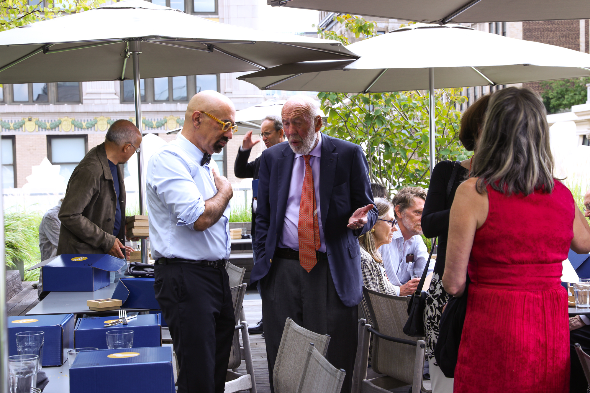 A photograph of a group of people in an outdoor space with seats and umbrellas.