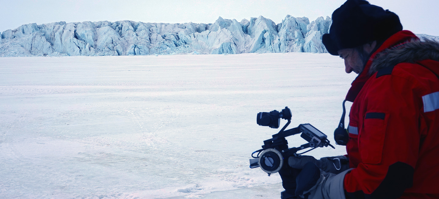 A man in a snow environment uniform with a mechanical device in an arctic landscape.