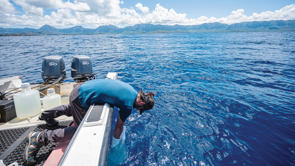 A photograph of a person riding a boat in the ocean and reaching into the water.