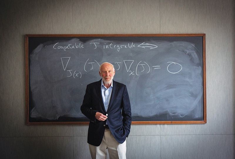 Jim stands in front of a chalkboard. A mathematical equation is written on the board.