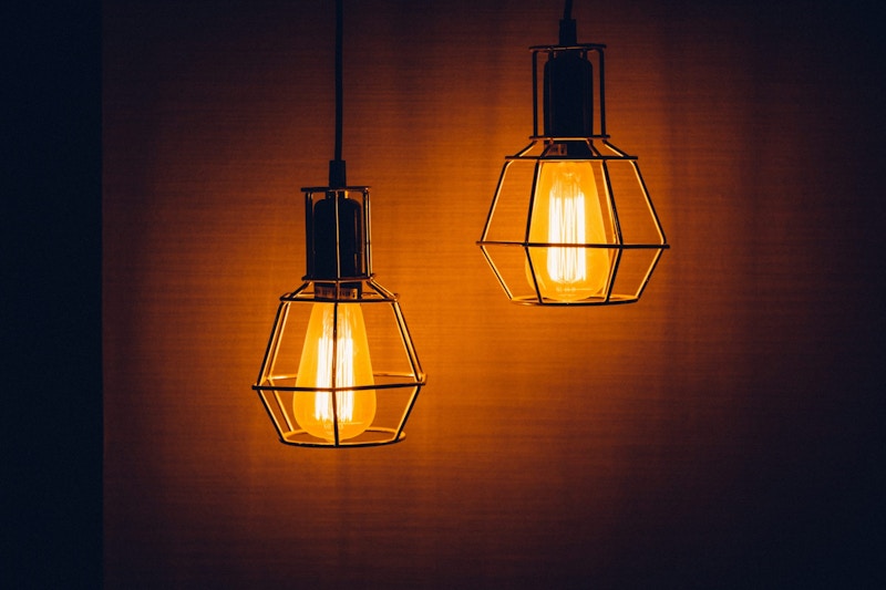 Two similar-looking lightbulbs shine while hanging from the ceiling.