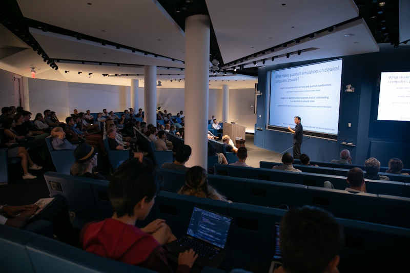 Man holding a pointer who is lecturing in front of a full room.