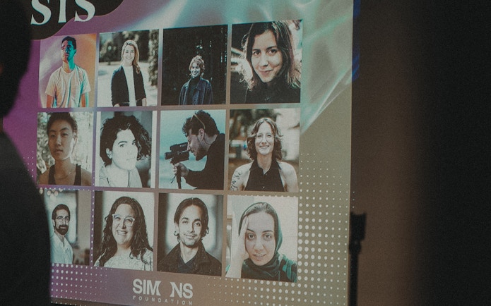 A photo taken at the screening of 'Symbiosis,' showing a dark auditorium with a film still of two clasped hands on the screen.