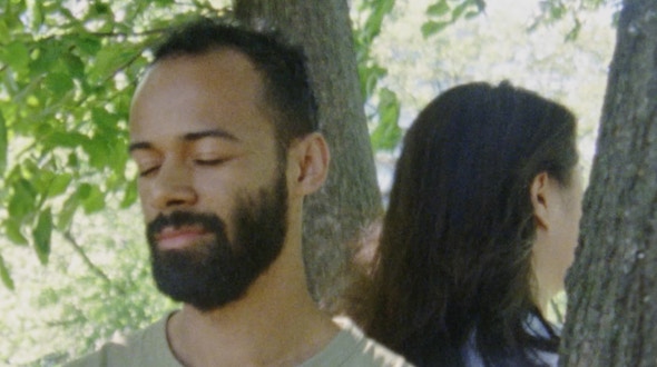 A man and woman standing back-to-back by a tree.