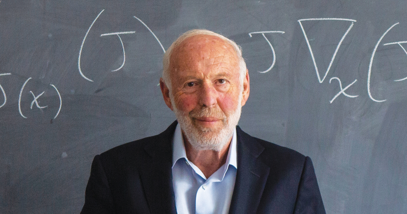 Jim Simons stands in front of a chalkboard. A mathematical equation is written on the board.