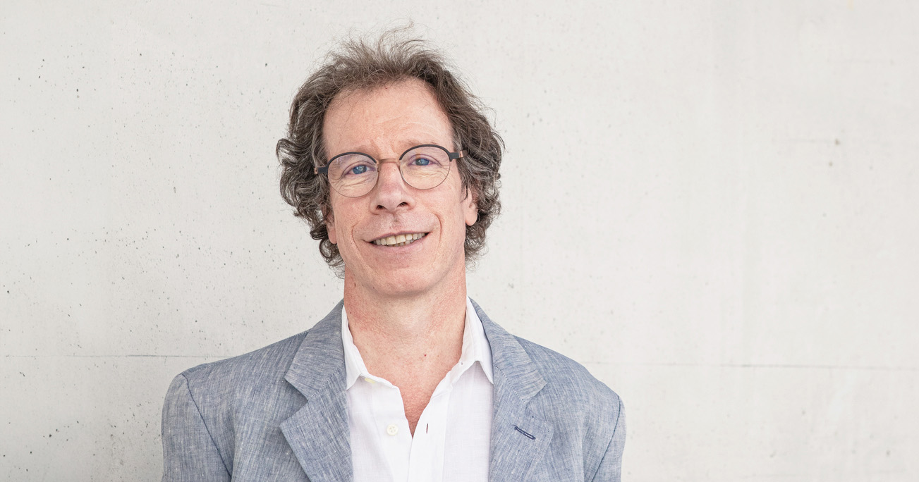 Portrait of Stéphane Mallat, winner of the 2025 CNRS Gold Medal, wearing a grey suit and leaning against a wall.