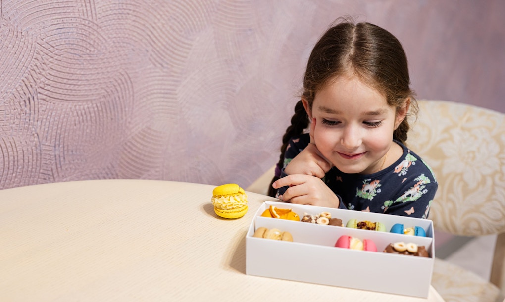 A photo of a little girl looking at a box of macarons, deciding which one to chaoose.