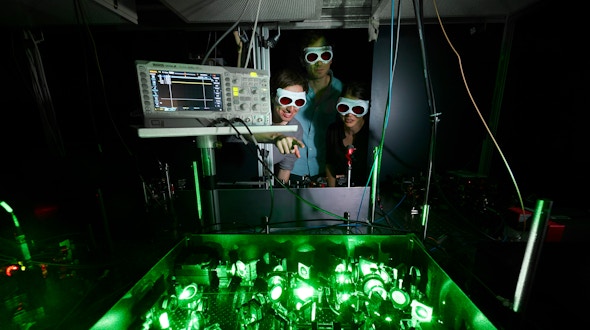 Photo of glowing green tabletop laser equipment with researchers looking on.