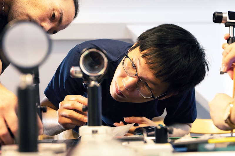 A photo of a student looking into a benchtop microscope.